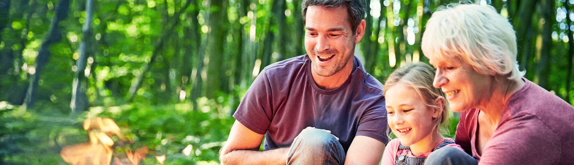 Multi-generation family roasting marshmallows at campfire in forest